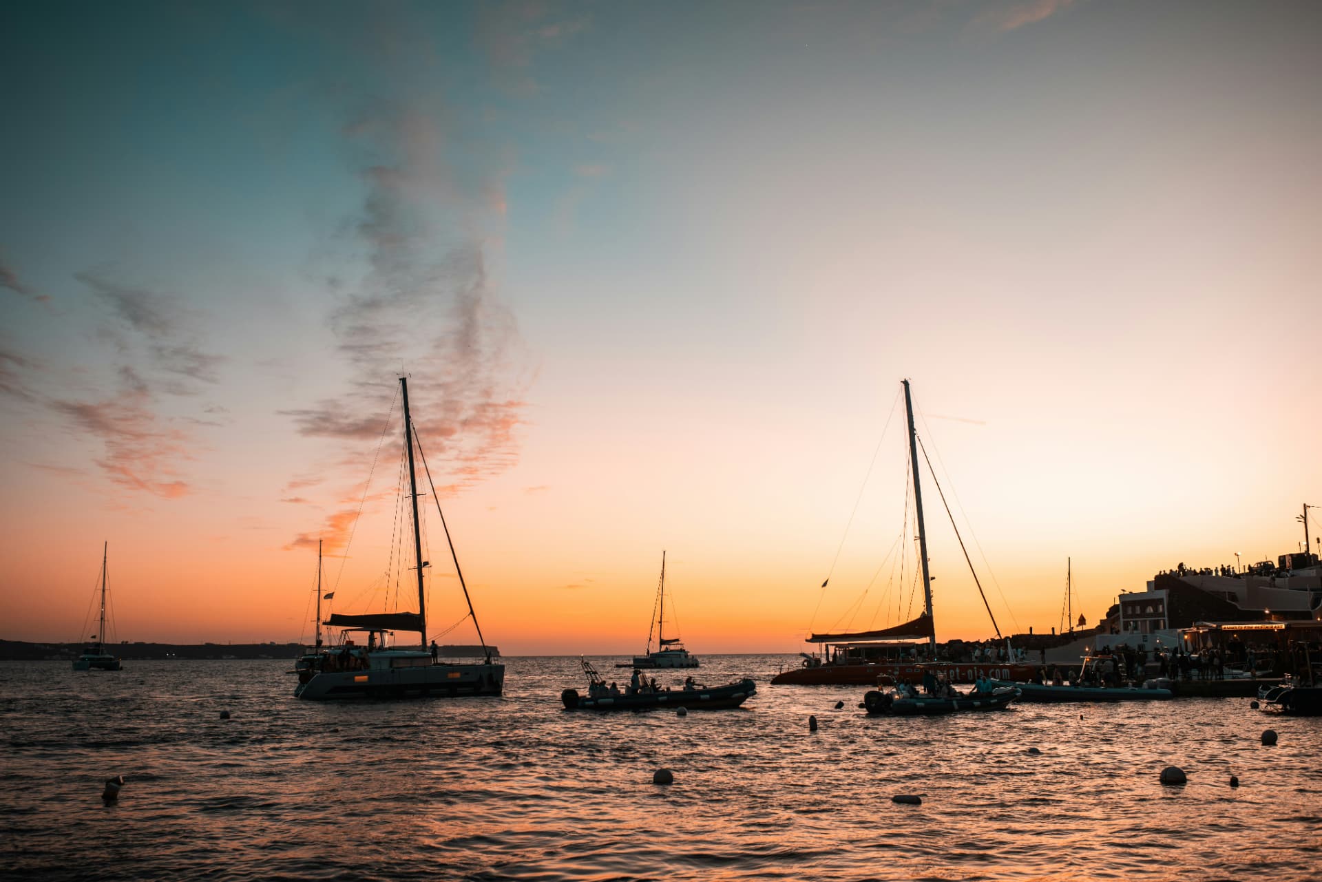 Sailboats resting on a calm harbour at sunset with the sky glowing orange and pink